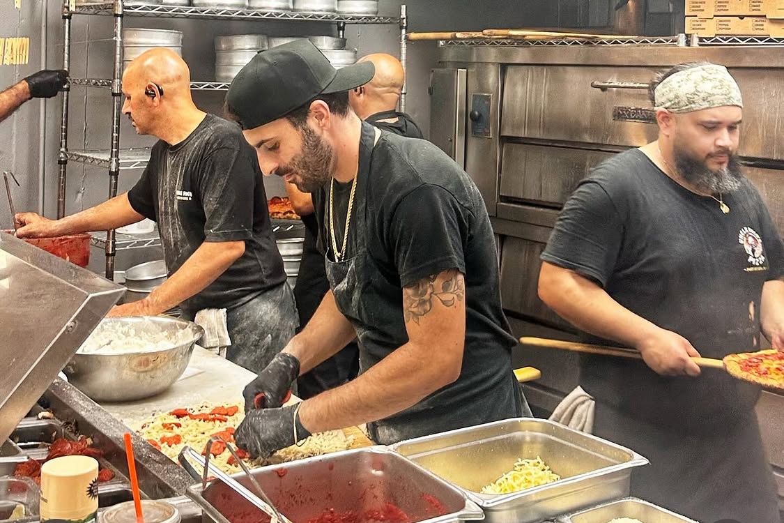 This photo shows several men making pizzas in the kitchen at Uncle Rico's.