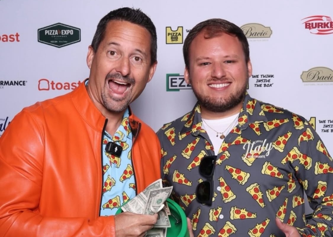 This photo shows Matt Plapp, pulling cash money out of a plastic bowl, and smiling for the camera with Avery Ward of Little Italy Ristorante.