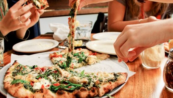 This photo shows customers' hands pulling slices out of a gourmet pizza.