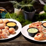 This photo shows Mellow Mushroom's Mellow Rollz and Pretzel Bites in separate plates along with cups of dipping sauce.
