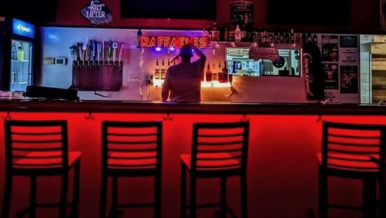 This photo shows the interior of Raffaeles Pizza, darkly lit, with a shadowy man standing behind the bar with his back to the camera.