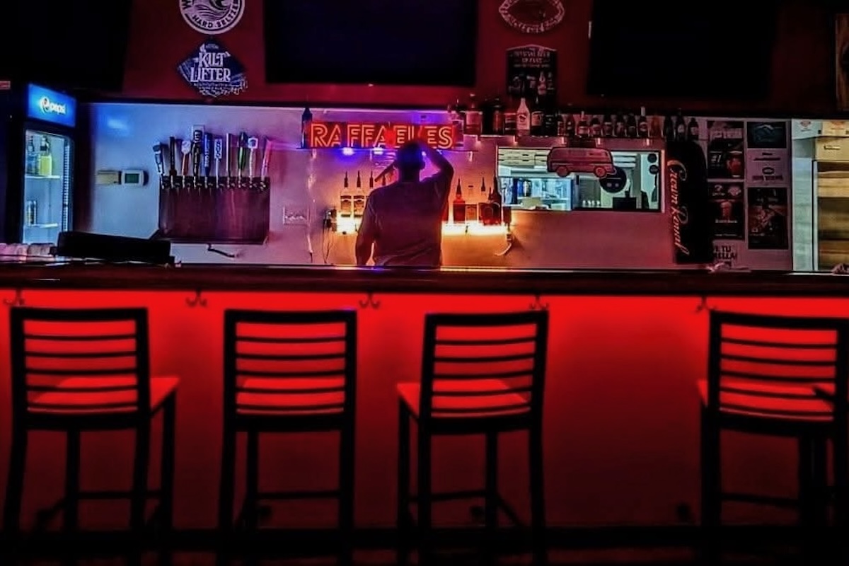 This photo shows the interior of Raffaeles Pizza, darkly lit, with a shadowy man standing behind the bar with his back to the camera.