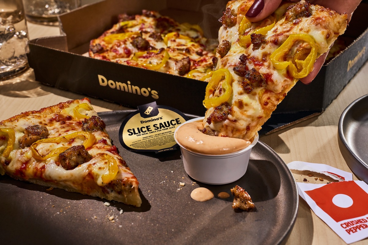 This photo shows a tasty-looking pizza slice being dipped into a little cup of the Slice Sauce.