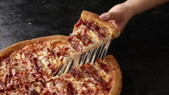 This photo shows a person's hand removing a slice from a triple bacon pizza from Papa Johns.