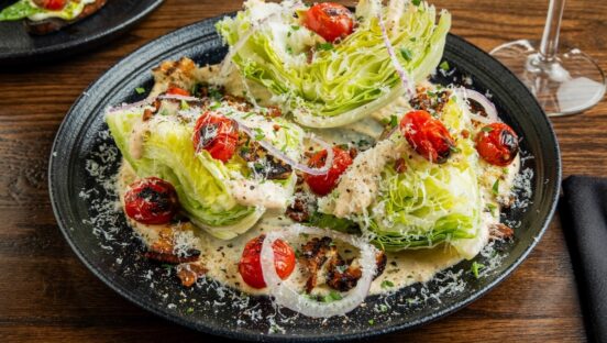 This photo shows a beautiful wedge salad with large wedges of iceberg lettuce, roasted cherry tomatoes and onions.