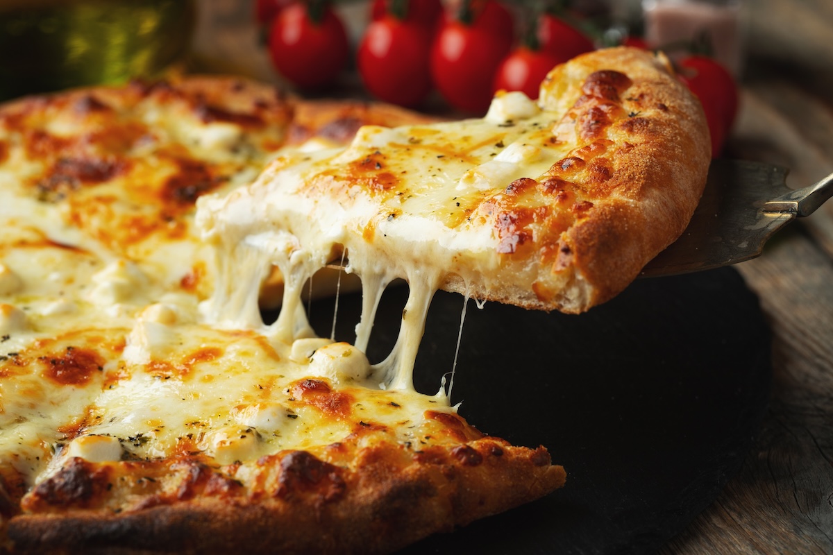 This photo shows a slice of pizza being extracted from a whole pizza topped with four different cheeses.