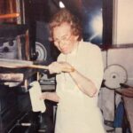 This washed out vintage photo shows Audrey Anderson looking at the camera as she peels a pizza into her oven.