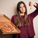This photo shows a young woman holding a pizza delivery box and giving the thumbs-down sign.