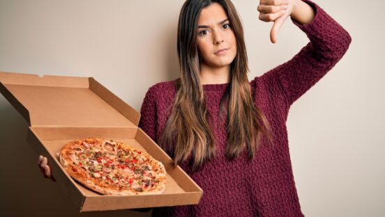 This photo shows a young woman holding a pizza delivery box and giving the thumbs-down sign.