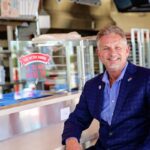 This photo shows Brian Bailey sitting inside his 100th Domino's store and smiling proudly.