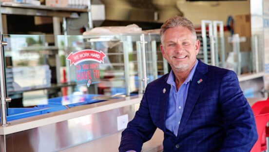 This photo shows Brian Bailey sitting inside his 100th Domino's store and smiling proudly.