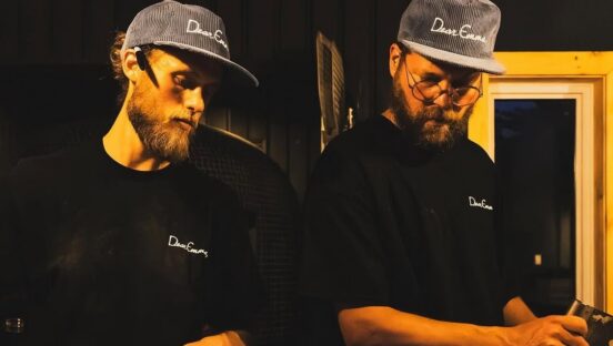 This photo, shot with dark moody lighting, shows Silvio and Paul working side by side making pizza in the kitchen at Dear Emma.
