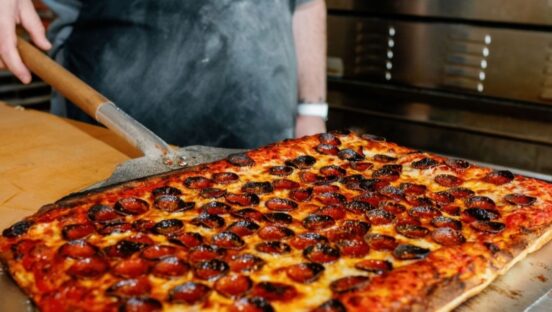 This photo shows a delicious looking rectangular pizza topped with pepperoni.
