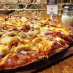 This photo shows a pizza topped with shredded chicken, red onions and fire-roasted tomatoes.