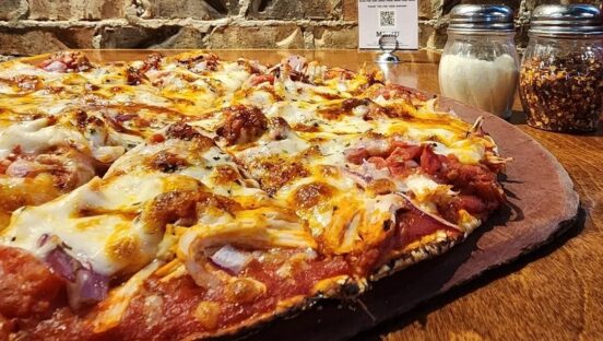 This photo shows a pizza topped with shredded chicken, red onions and fire-roasted tomatoes.