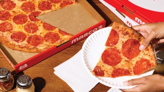 This photo shows a woman's hands holding a slice of New York-style pepperoni pizza in a paper plate.