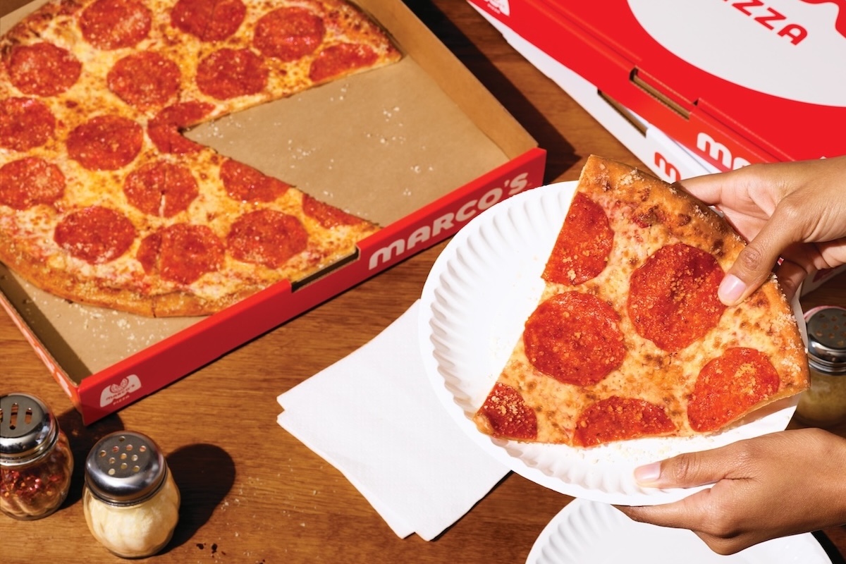 This photo shows a woman's hands holding a slice of New York-style pepperoni pizza in a paper plate.