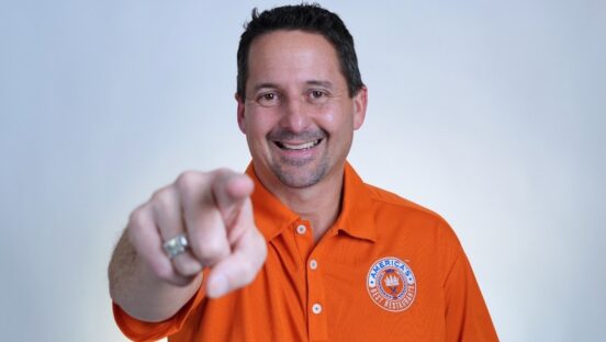 This photo shows Matt Plapp in his trademark orange shirt smiling and pointing confidently at the camera.