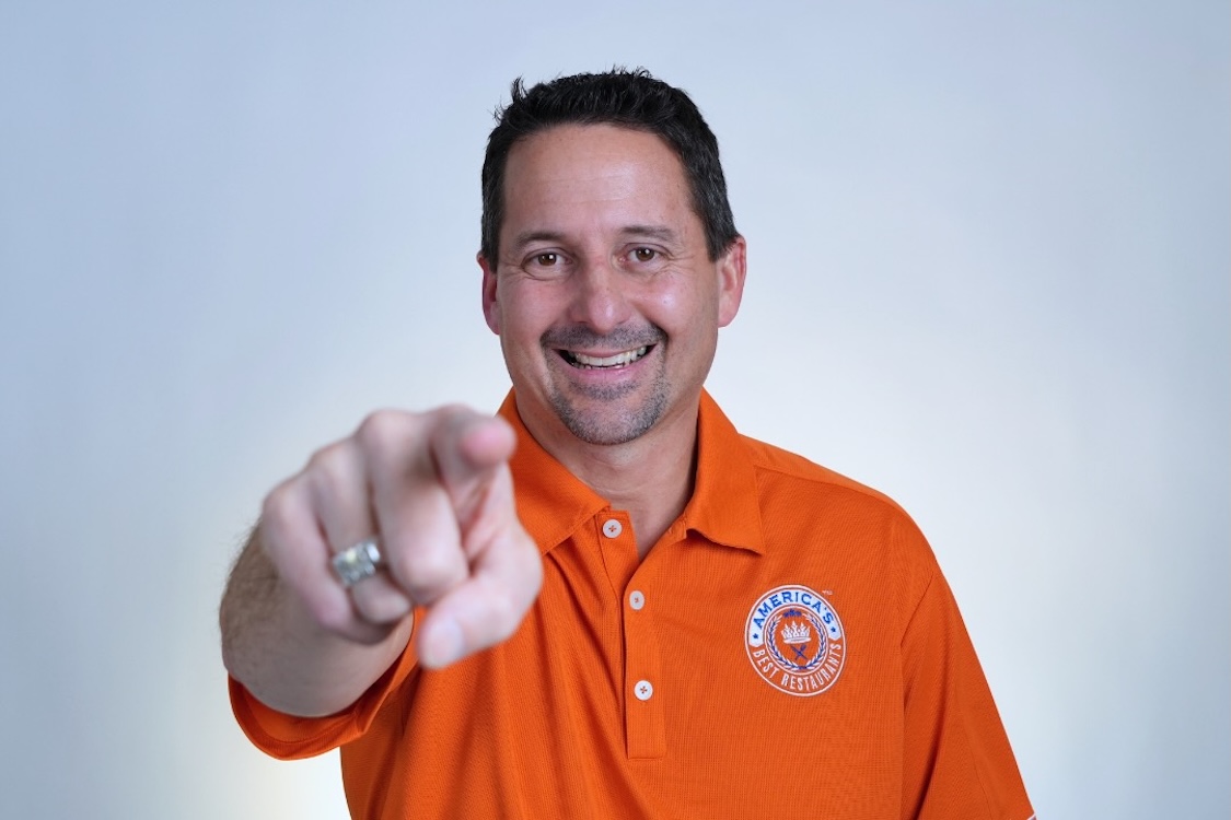 This photo shows Matt Plapp in his trademark orange shirt smiling and pointing confidently at the camera.
