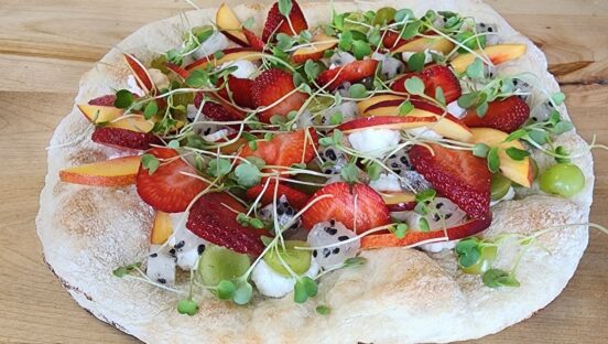 This photo shows a pizza topped with sliced strawberries, grapes, peaches and more.