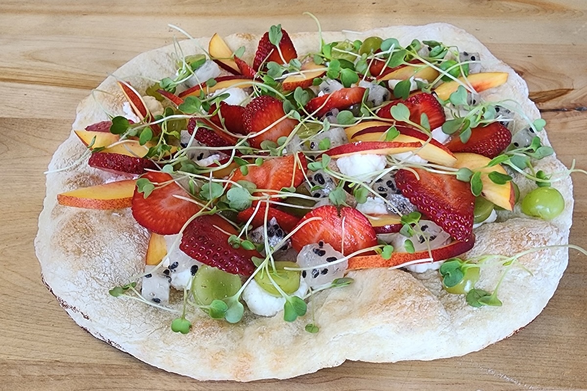 This photo shows a pizza topped with sliced strawberries, grapes, peaches and more.