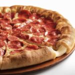 This photo shows a whole stuffed crust pizza from Pizza Hut, with cheese oozing out from a slice in the foreground.