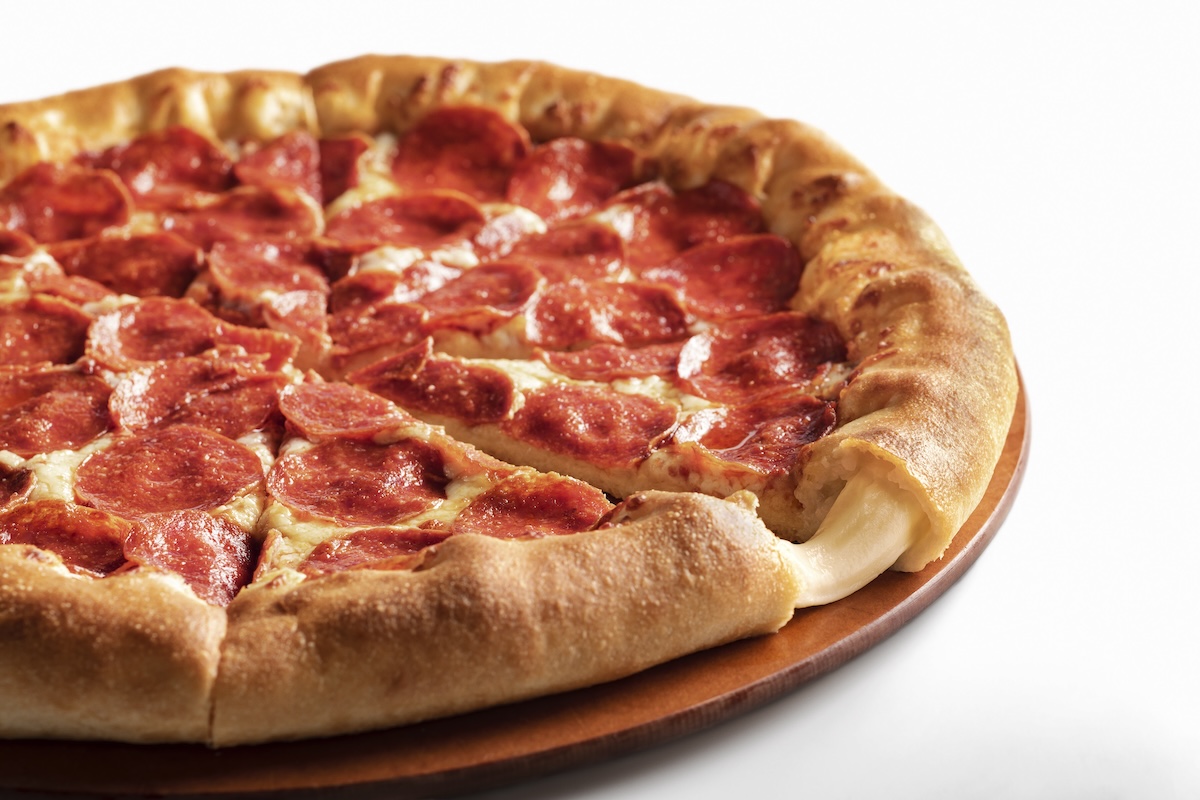 This photo shows a whole stuffed crust pizza from Pizza Hut, with cheese oozing out from a slice in the foreground.