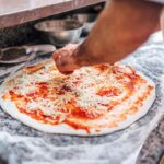 This photo shows a chef adding cheese to a pizza base.