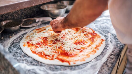 This photo shows a chef adding cheese to a pizza base.