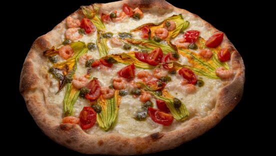 This photo shows a pizza topped with squash flowers, shrimp, tomatoes and mozzarella cheese.