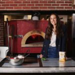 Alexandra "Azie" Mortati of Orlando Foods and Women in Pizza poses in front of a pizza oven.