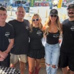 This photo shows the owner of Brooklyn Square Pizza lined up with two young men and two young women all wearing black t-shirts with the brand's logo.