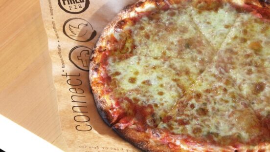 This photo shows a baked cheese pizza placed on top of branded Fired Pie paper.