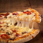 This photo shows a Hot pizza slice with melting cheese on a rustic wooden table.