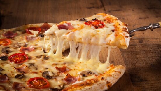 This photo shows a Hot pizza slice with melting cheese on a rustic wooden table.