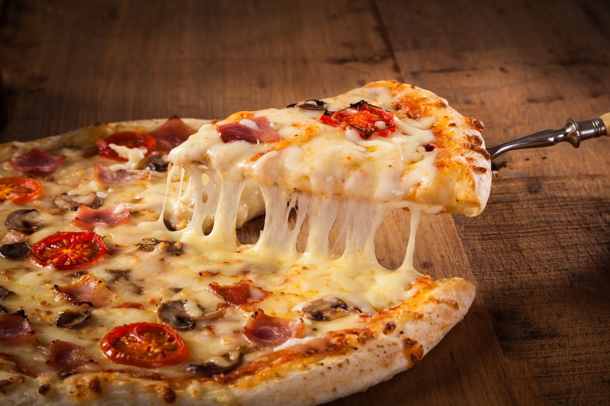 This photo shows a Hot pizza slice with melting cheese on a rustic wooden table.