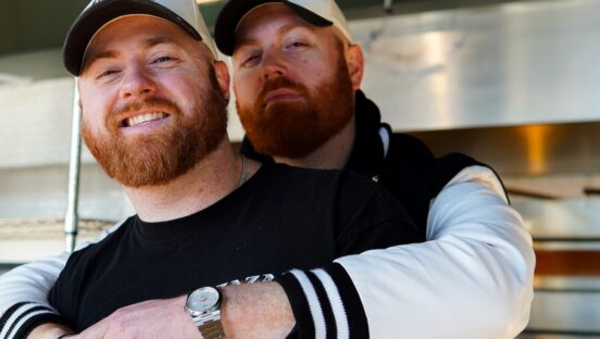 This photo shows the two brothers together. Chadd is standing behind Brett and has his arms wrapped affectionately around Brett's shoulders. Both men are smiling.