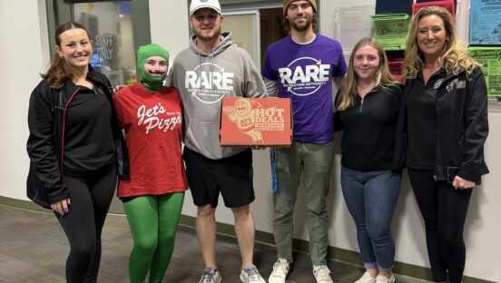 This photo shows Jet's Pizza team members, including on person dressed as the Jet's mascot, presenting a boxed pizza to representatives of RARE (Recreation Authority Roseville & Eastpointe)