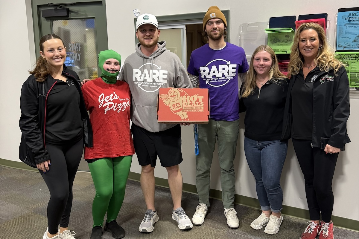 This photo shows Jet's Pizza team members, including on person dressed as the Jet's mascot, presenting a boxed pizza to representatives of RARE (Recreation Authority Roseville & Eastpointe)