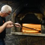 This photo shows Bill Pustari moving a pizza around his coal-fired oven with a peel.