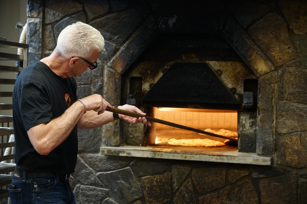 This photo shows Bill Pustari moving a pizza around his coal-fired oven with a peel.