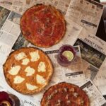 This photo shows the three mobster-themed pizzas arranged over mock newspapers with headlines about Next Door Bar.