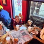 This photo shows a woman and two little girls at Big Apple Pizza. The two children are all smiles, and the girl on the right is excitedly holding up a slice of pizza.