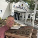 This photo, a selfie, shows Scott VanDuzer smiling and holding a bunch of pizza boxes as he stands in front of St. Lucie Elementary School.