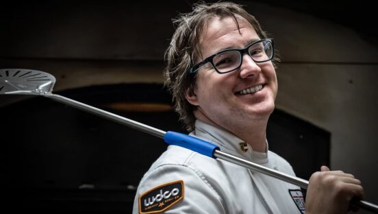 This phots shows Sean Dempsey smiling in his white USPT chef jacket with a metal peel slung over his shoulder.