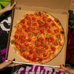 This photo shows two pairs of hands holding a box containing the Shredders Revenge pizza described in the story.