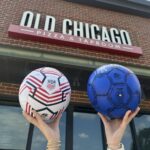 Customers hold soccer balls in front of Old Chicago Pizza + Taproom