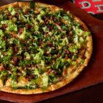 This photo shows the Caesar pizza topped with lettuce, Romano cheese and bacon.
