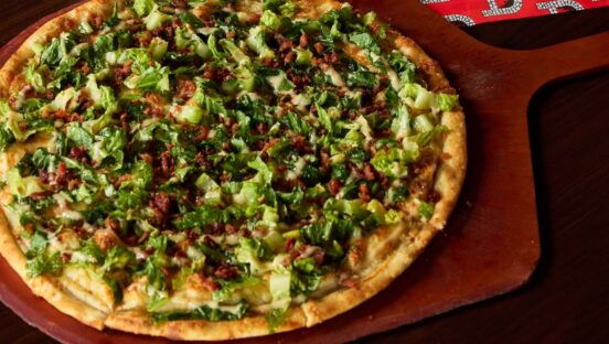 This photo shows the Caesar pizza topped with lettuce, Romano cheese and bacon.