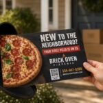 This photo shows a man's hand holding a direct mail postcard with a photo of a pizza and a headline that reads: New to the Neighborhood? Your First Pizza Is On Us." The postcard is held up against an outdoor mailbox.